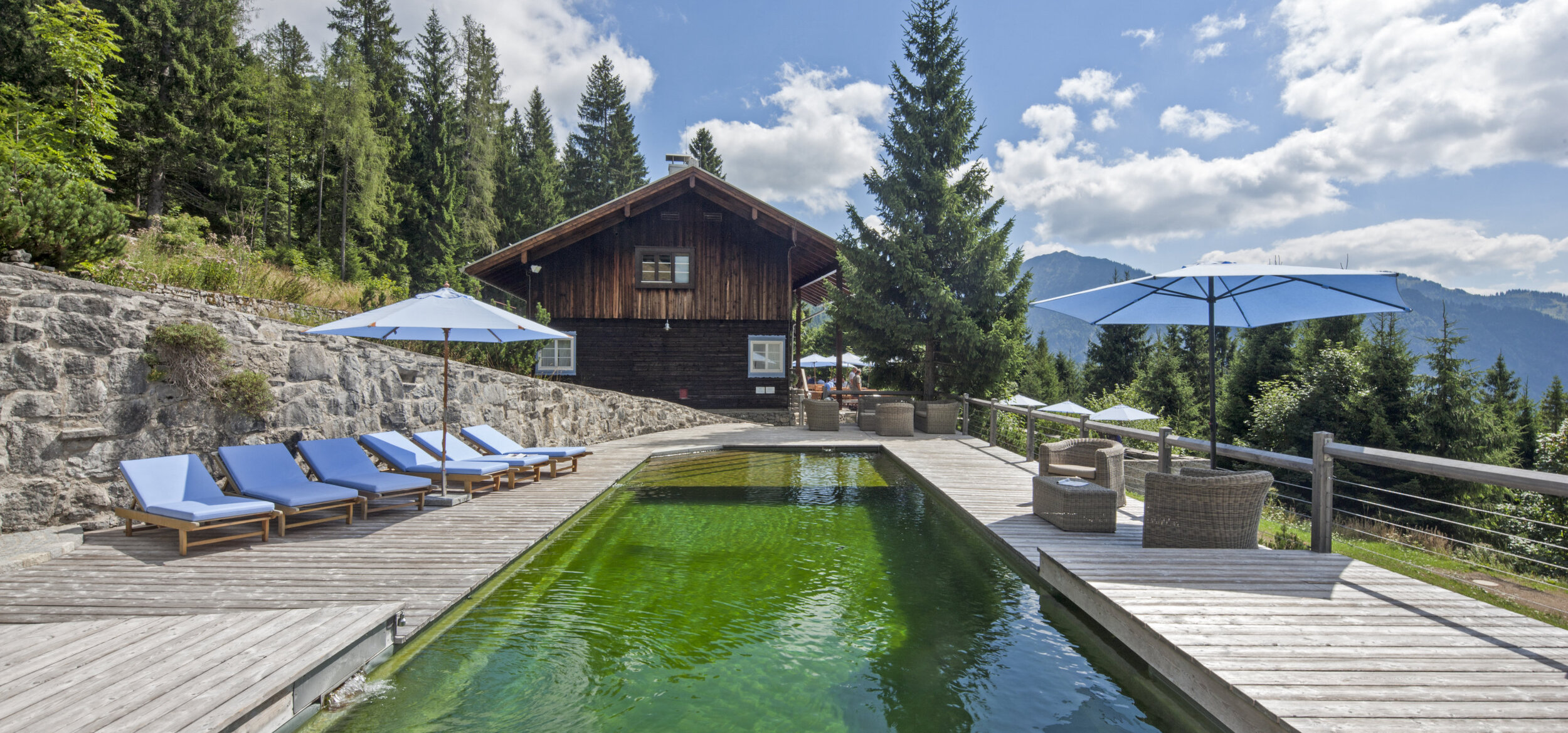 Natural pool with Balena system with loungers at the “Silberghaus” hotel spa in Bayrischzell, with the Alps in the background